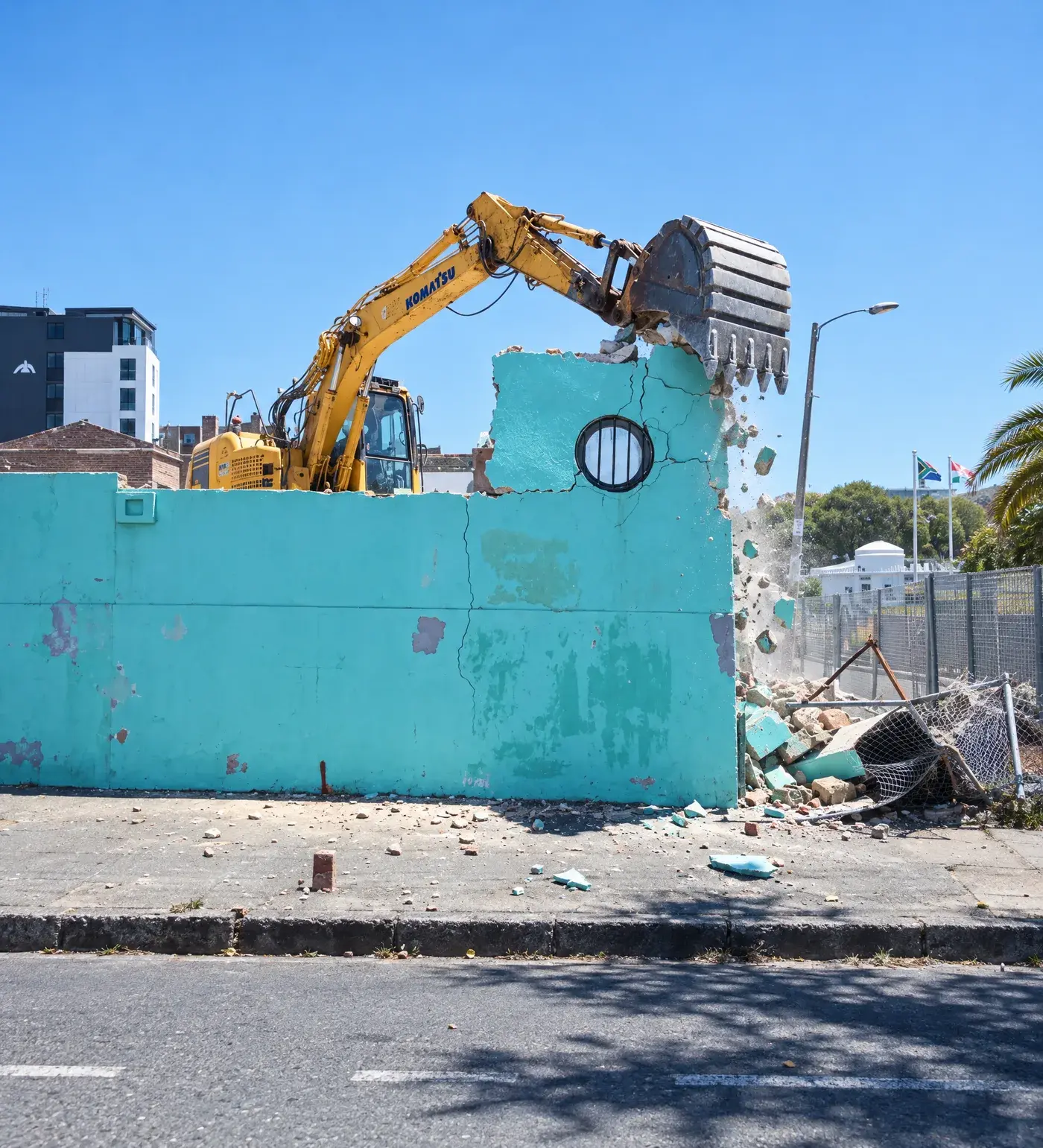 Komatsu excavator knocking down a turquoise boundary wall on a Cape Town city site