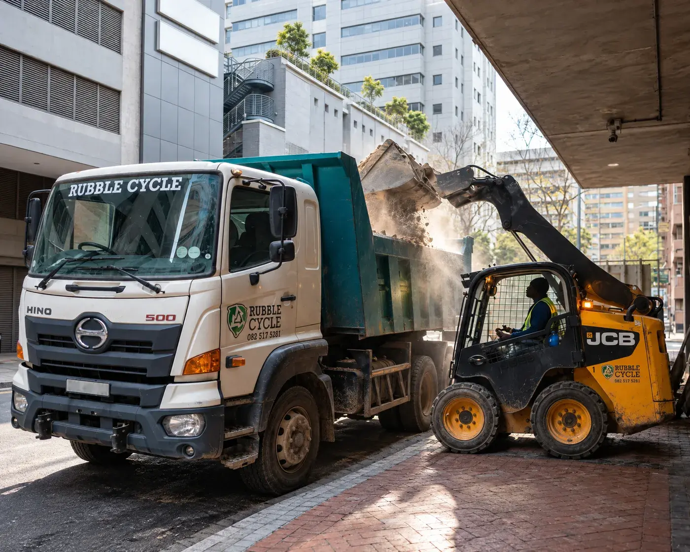 JCB skid steer tipping soil into a Rubble Cycle Hino tipper truck on a Cape Town city street